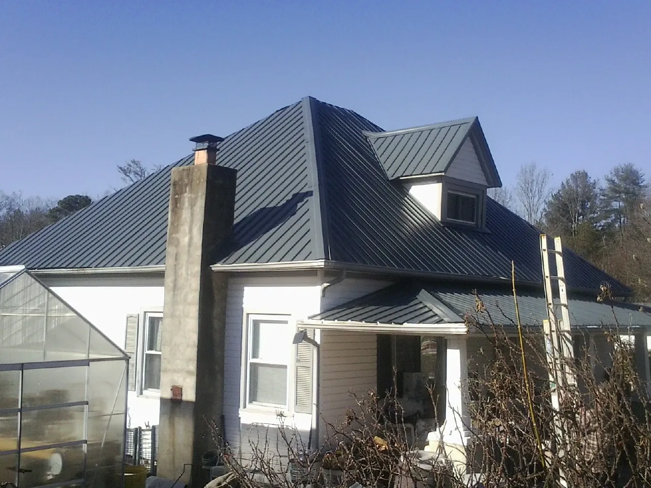 Dark blue standing seam metal roof on a white farmhouse with dormer — Slate & Tile Roof Repair by Roofing Brothers in Volga
