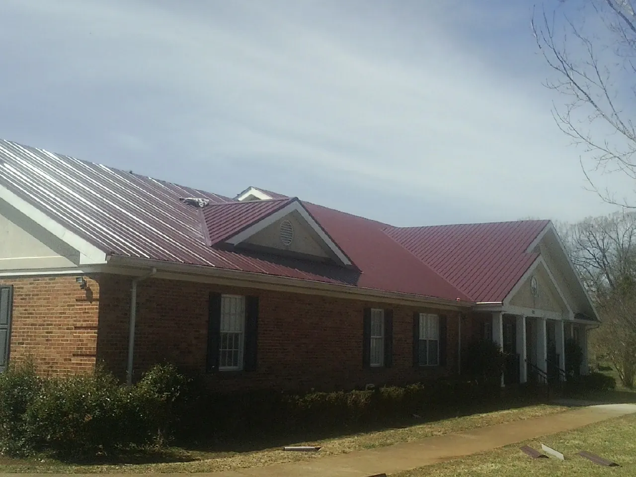 Red metal roof with gabled entries on a long brick building, from a Hail Damage Roof Repair job in Volga
