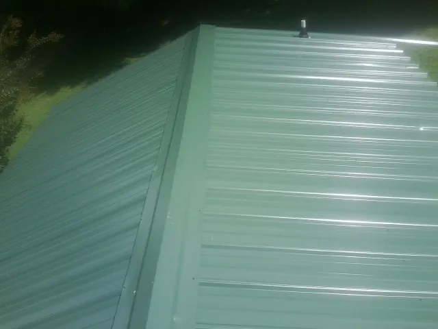 New green metal panels meeting at the ridge of a roof — Flat Roof Repair work by our crew in Volga