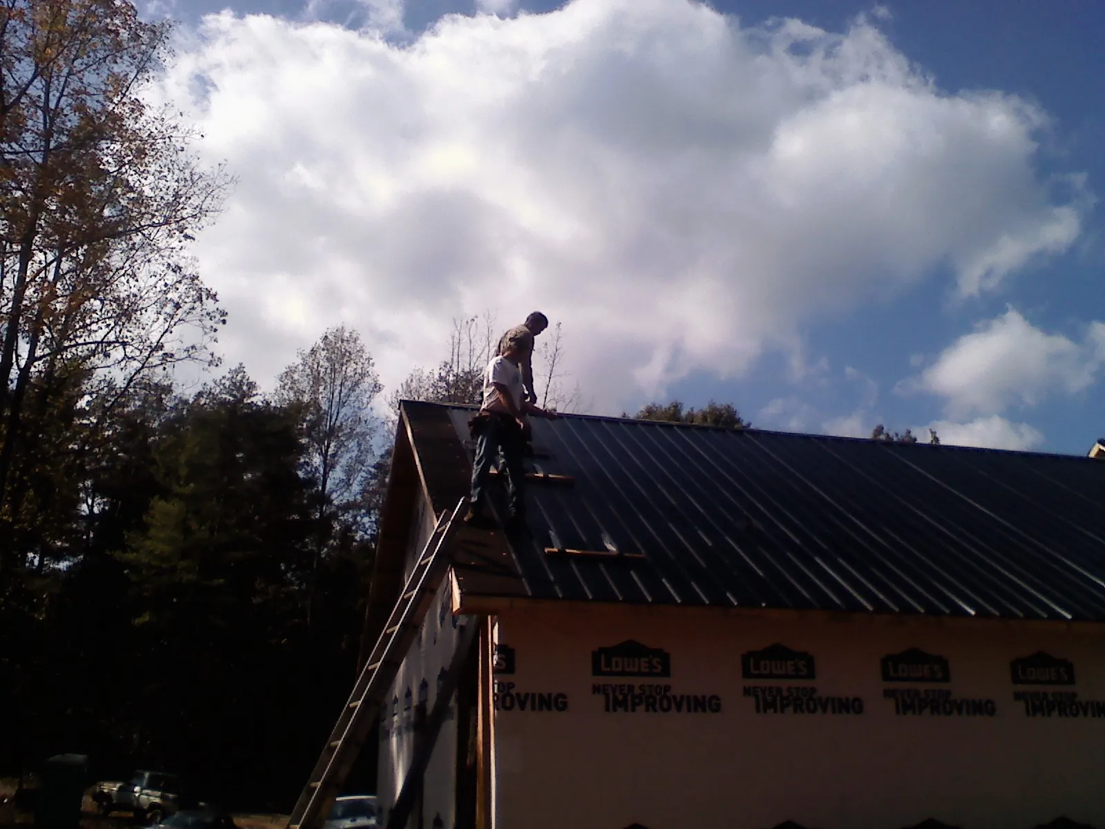 Roofer fastening dark metal panels high against a cloudy sky, from a Roof Inspection job in Volga