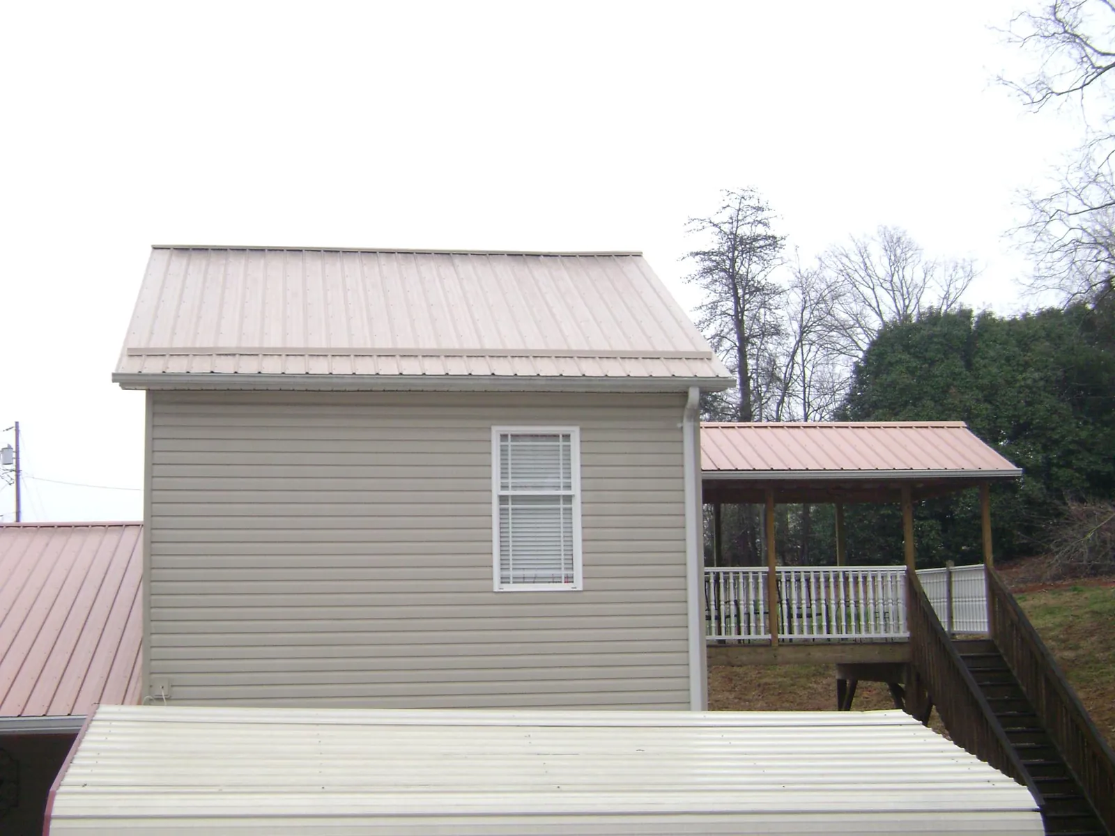 Tan metal roofs on a two story addition and attached porch, from a Roof Replacement job in Volga